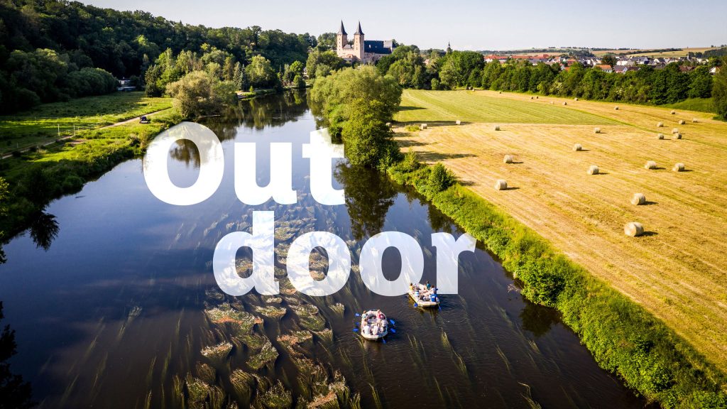Luftaufnahme von Paddelbooten auf der Zwickauer Mulde, flankiert von Feldern und Bäumen, im Hintergrund Schloss Rochlitz; großer Schriftzug ‚Outdoor‘ über dem Bild. Foto: BUR Werbeagentur GmbH
