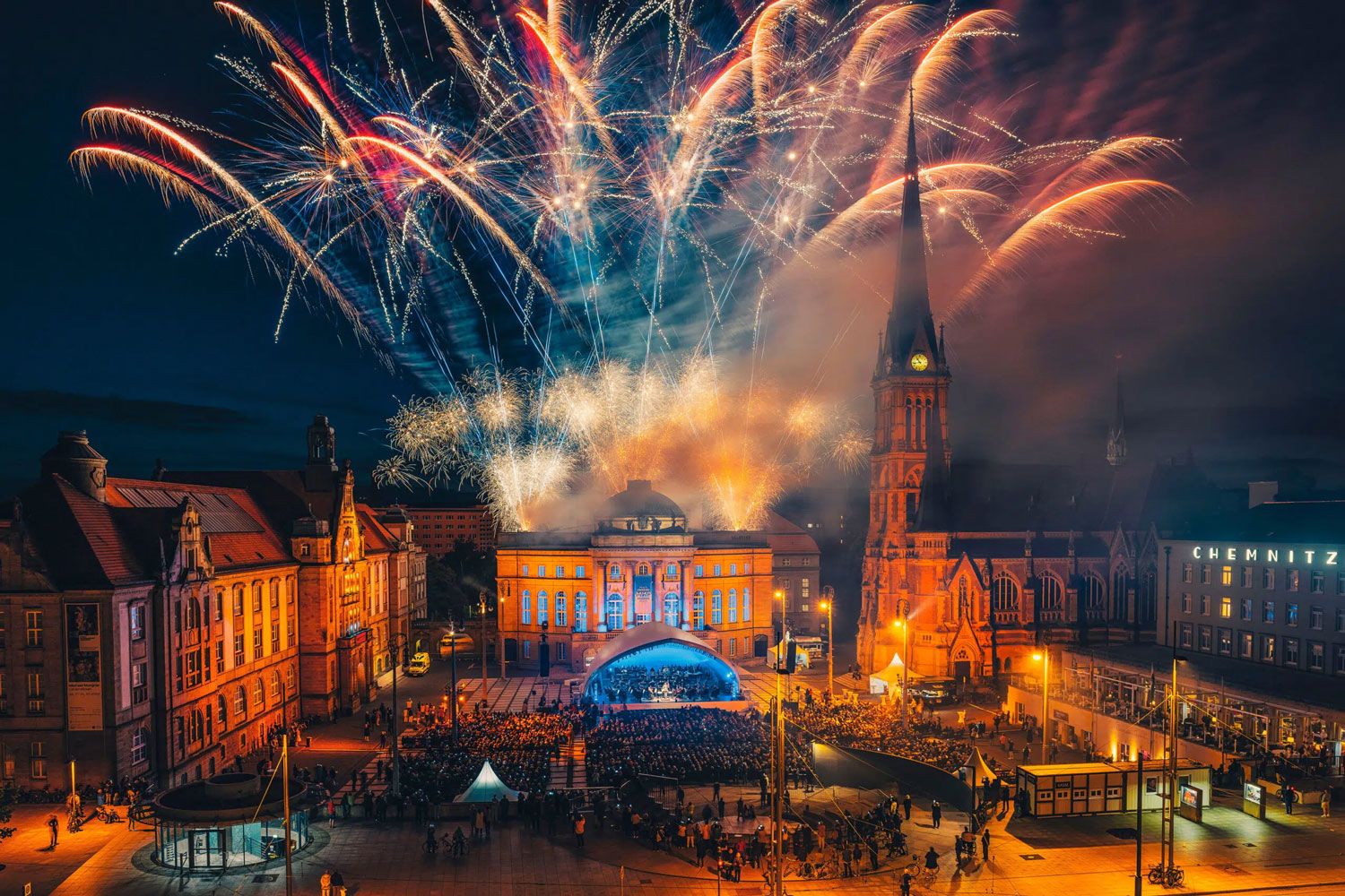 Der Theaterplatz in Chemnitz bei Nacht mit einem großen Feuerwerk am Himmel. Auf dem Platz findet eine Oper-Air-Veranstaltung mit vielen Gästen statt. Foto: Nasser Hashemi